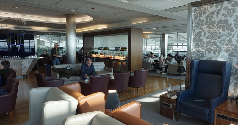 An airport terminal lounge with seating and large windows, where travellers wait between flights