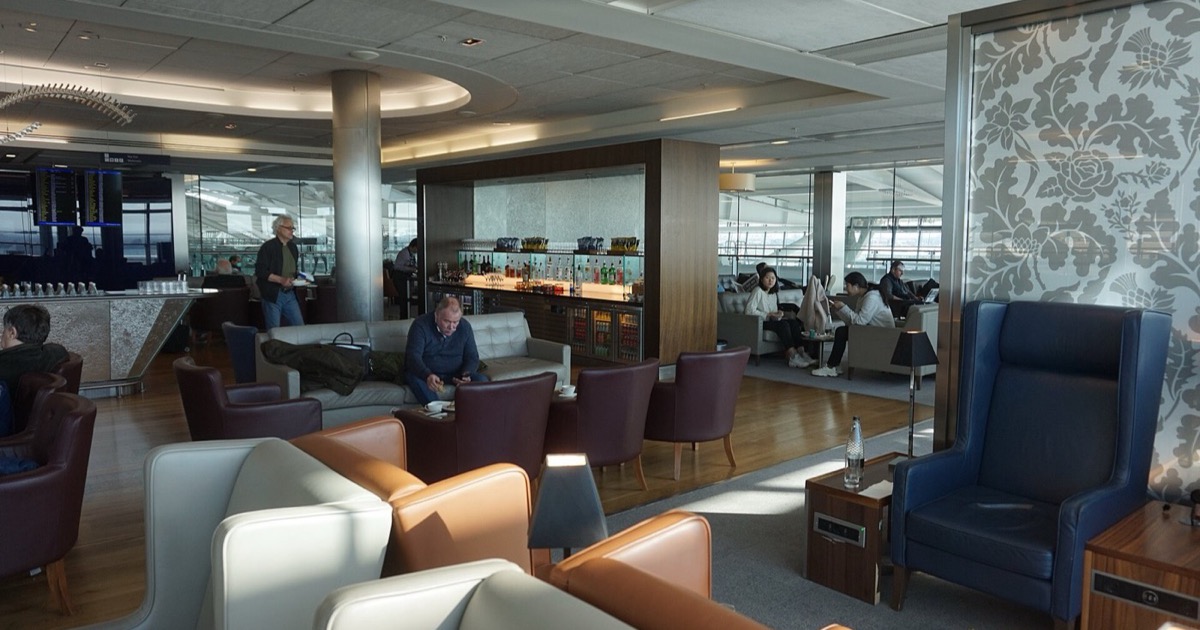 An airport terminal lounge with seating and large windows, where travellers wait between flights