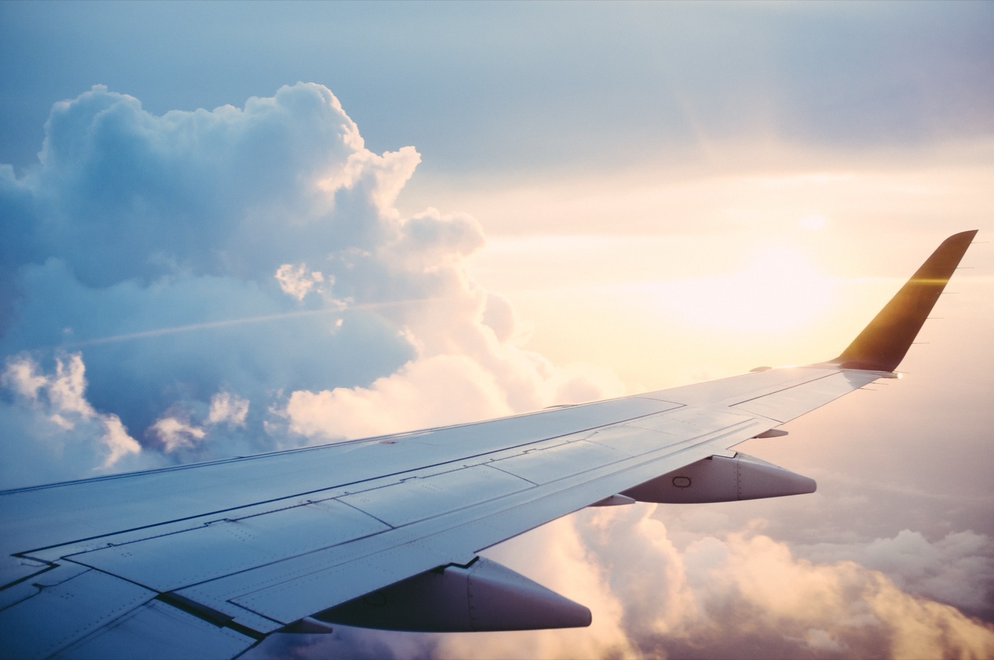 The wing of an airplane above clouds at golden hour, seen from a passenger window