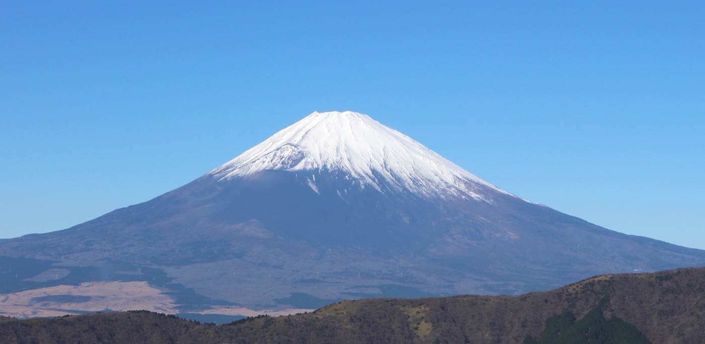 Snow-capped Mount Fuji against a clear blue sky, seen from the ground
