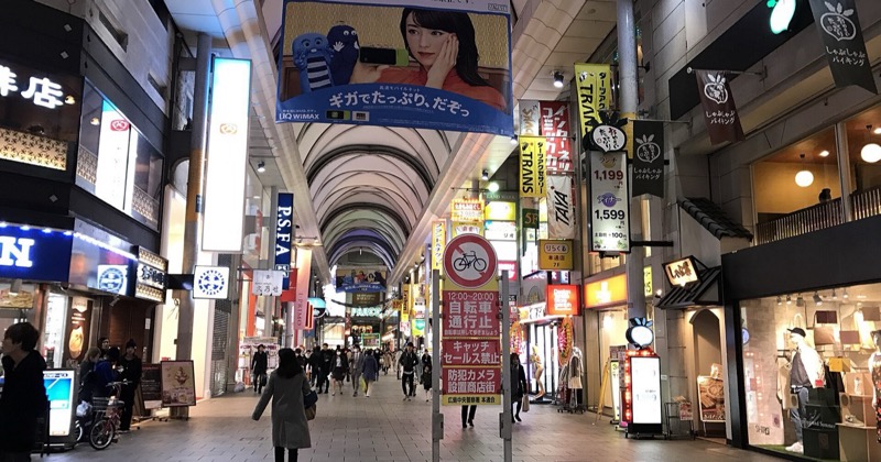 A covered shopping street in Hiroshima at night, lined with illuminated Japanese signage